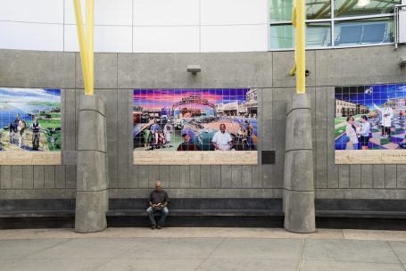 A man sitting on the ground in front of a large poster.